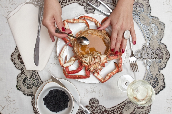 Woman hands is taking sauce from a big red cooked spider crab in a luxury dinner