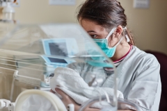 Female doctor holding newborn in incubator